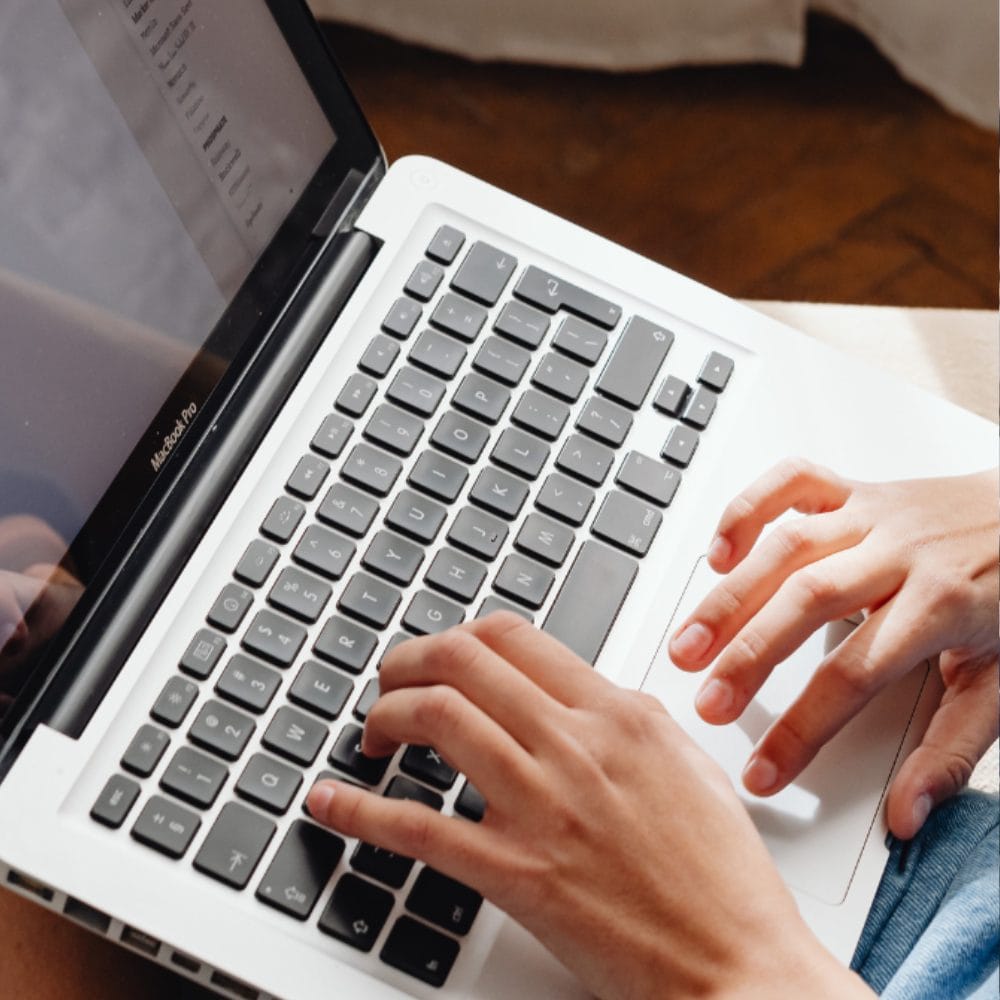 Close-up of a person’s hands typing on the keyboard of an open silver laptop, viewed from above. The partial screen displays text about Raiser's Edge options for nonprofits in a document.