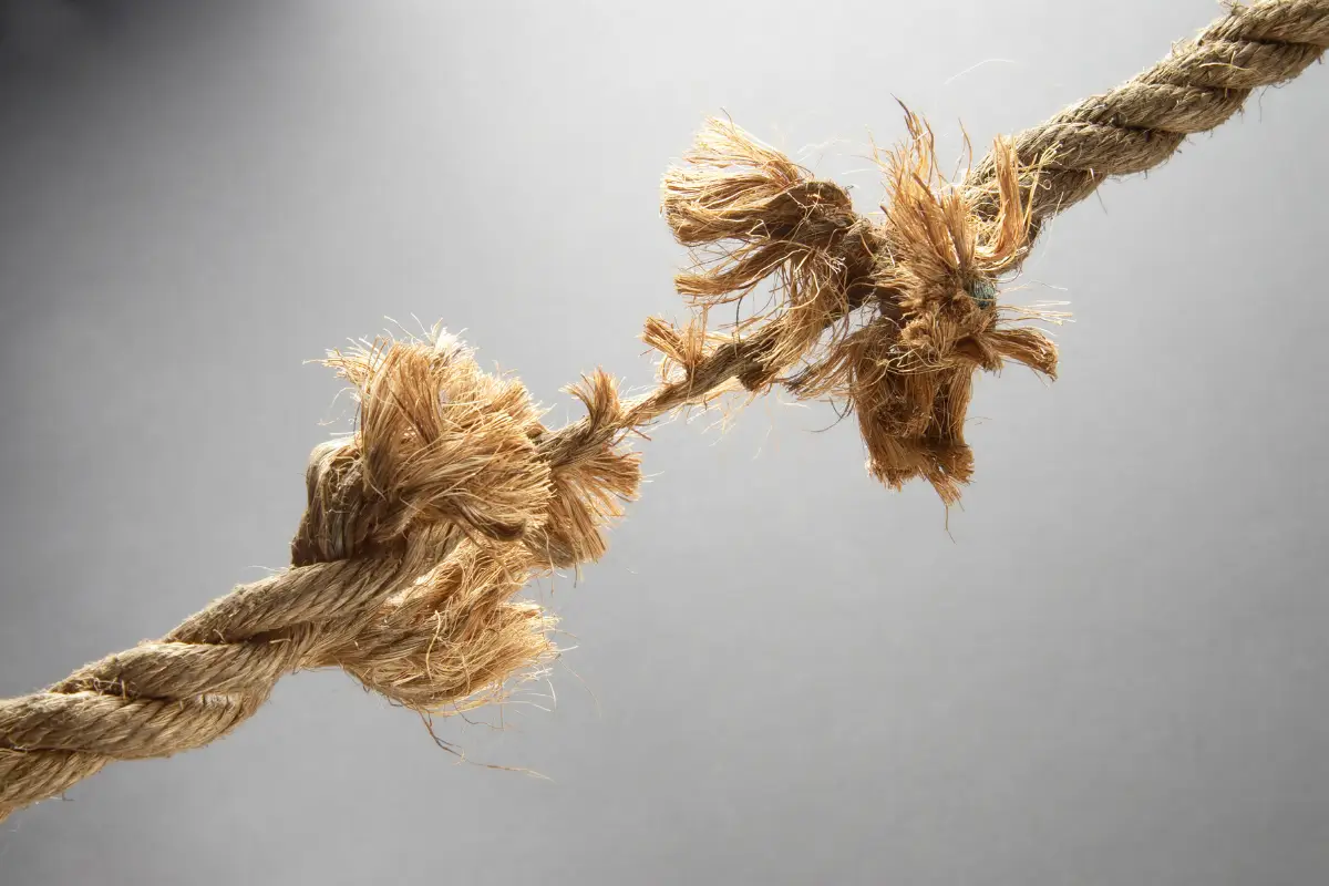 A close-up of a thick, frayed rope with strands coming apart against a neutral gray background, evoking tension—much like how technology exacerbates the nonprofit workforce crisis.
