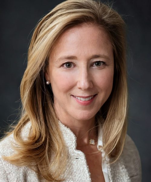 A woman with shoulder-length blonde hair wearing a light-colored textured blazer, a white blouse, and a small necklace, smiling in front of a dark background—perfect for an Andrew Abrams Senior Nonprofit Tech Consultant profile.